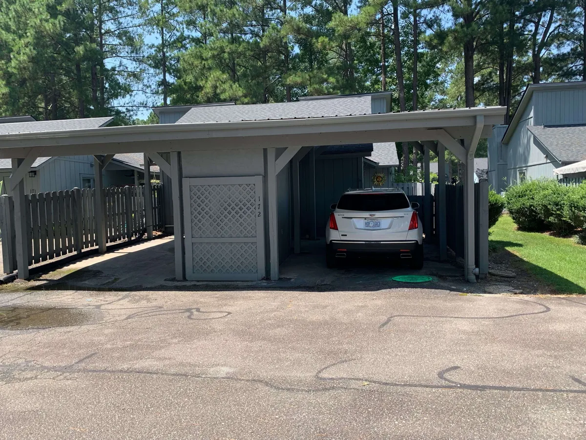 The image showcases a peaceful carport structure with a white vehicle parked beneath and greenery all around. The tranquil surroundings suggest leisure and ease, complementing the idea of a relaxed home environment ideal for families returning from local adventures.