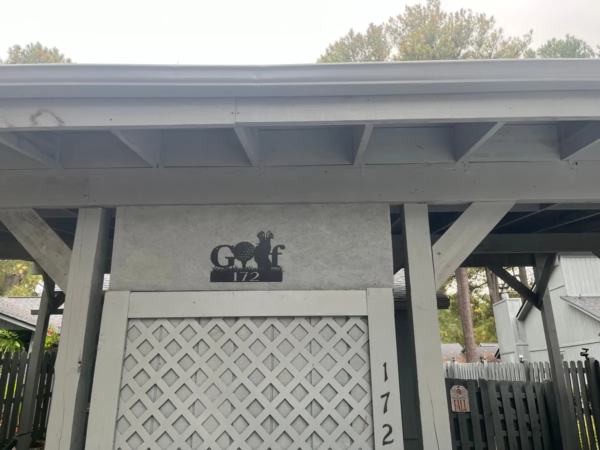 A sign for golf with the number 172 is prominently displayed, set against lattice-work and surrounded by mature trees and structures. The welcoming scene hints at the well-established and friendly nature of the community.