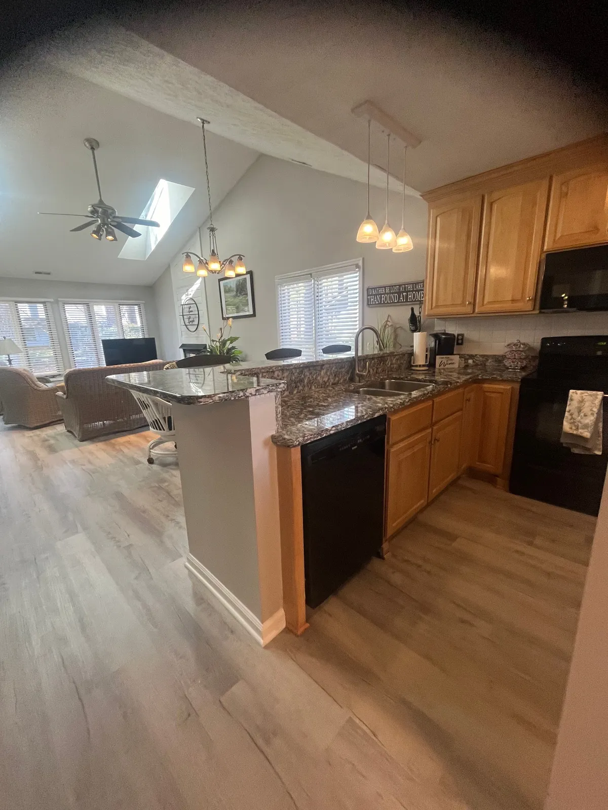 A warm kitchen view featuring a spacious granite countertop, rich wooden cabinetry, and contemporary lighting. The open layout connects the kitchen to the rest of the living area, reinforcing its central location and the flow between cooking and socializing. The setting suggests both early-morning rituals and festive family meals.