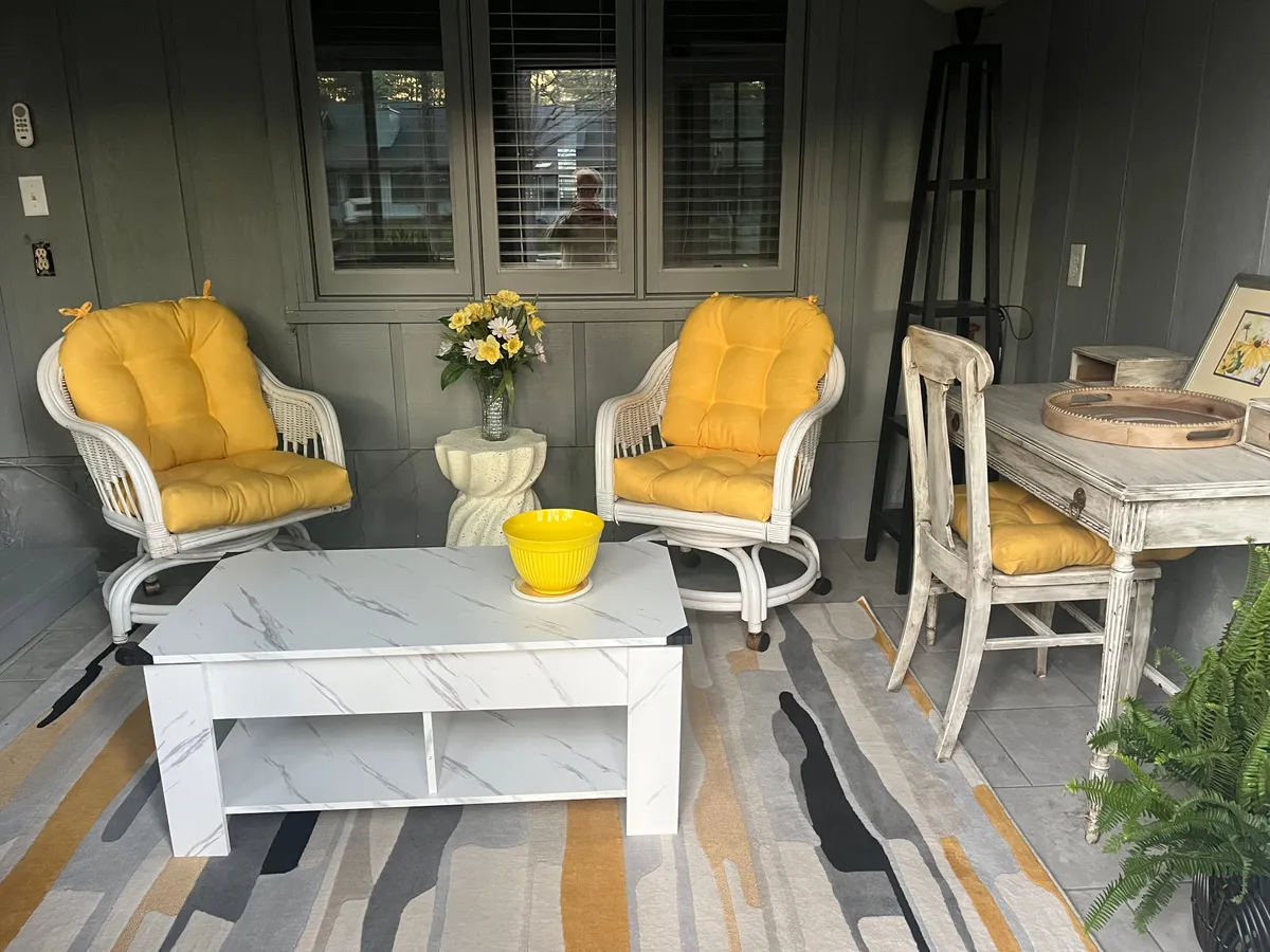An open living and dining area featuring yellow chairs, a coffee table with a floral arrangement, and a dining table in view. The layout is bright and cheerful, seamlessly connecting lounging and dining zones, with ample space and decor for both casual and festive moments.