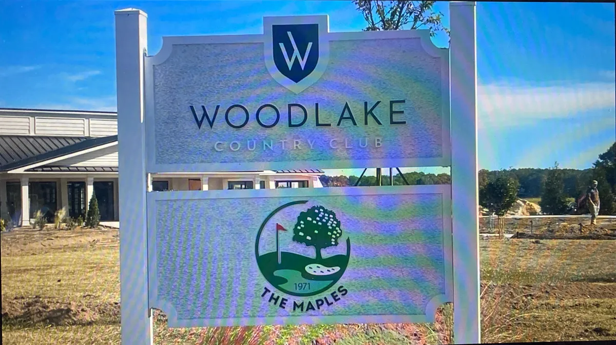 A distinguished sign for Woodlake Country Club with The Maples logo, set against a backdrop of manicured lawns and mature trees, hinting at the vibrant club life and outdoor events within the community.