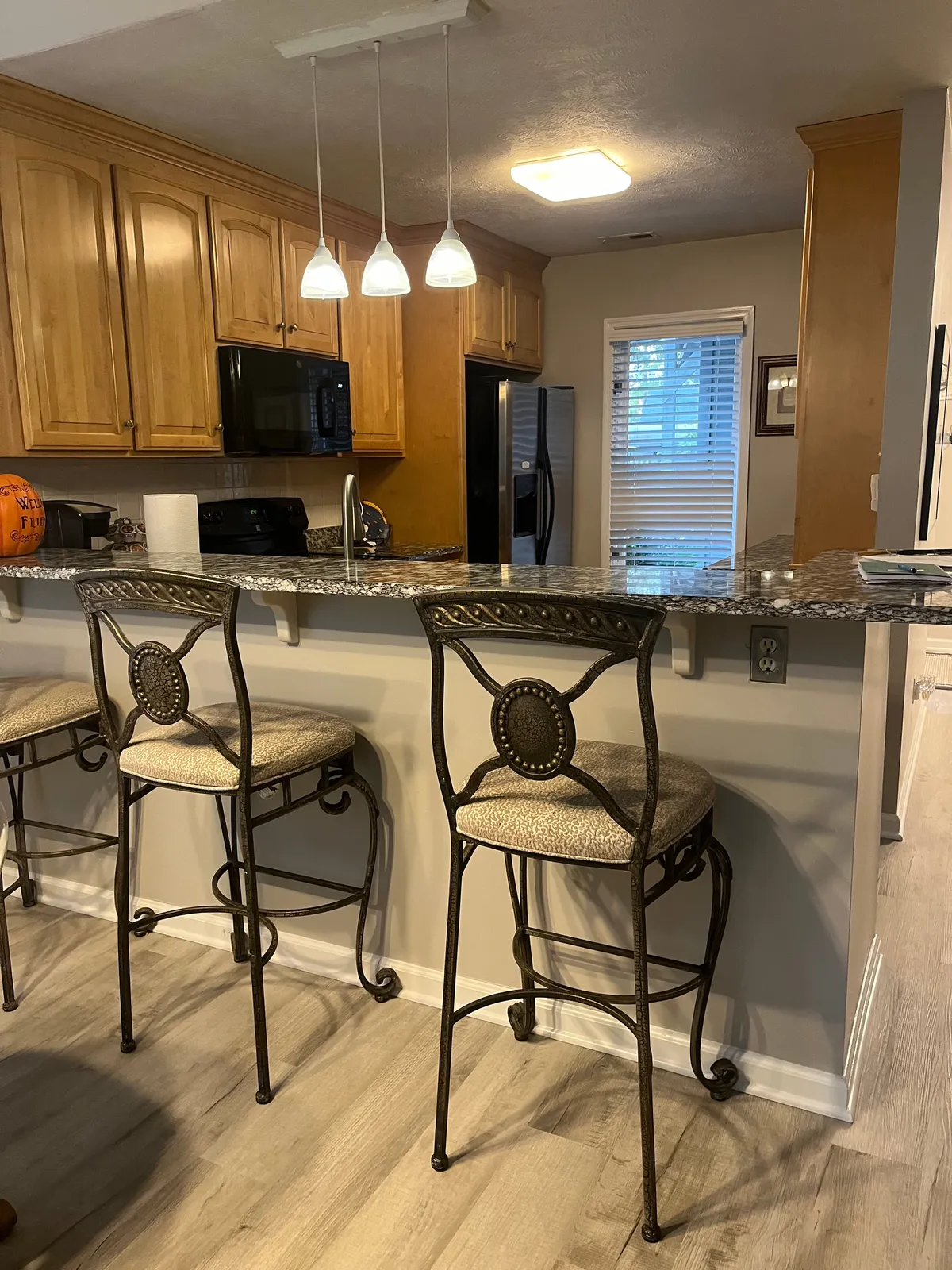 This image showcases a central kitchen island with granite countertops, stylish pendant lighting, and bar stools that invite guests to gather around. The space is bright and welcoming, suggesting a lively atmosphere where cooking and socializing seamlessly blend. The modern appliances are subtly visible, reinforcing the well-equipped nature of the kitchen.