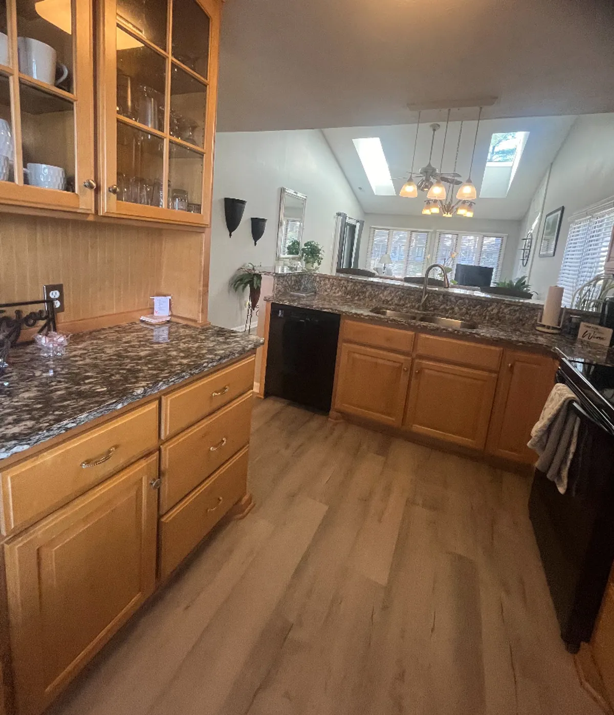 A cozy kitchen scene spotlighting granite countertops, warm wood cabinets, overhead skylights, and a range of modern appliances. The image hints at both everyday cooking and special-occasion gatherings, with an inviting, homey vibe.